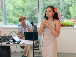 Jazmine, one of this year's SunRYSE students, in a beige dress speaking into a microphone.